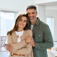 Smiling affectionate loving middle aged couple, happy romantic mature older Latin man and woman in their 50s hugging looking at camera standing together in modern kitchen at home. Portrait.