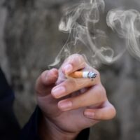 Closeup hand holding lighted cigarrette of asian smoking boy in private area of school and house to avoid punishment from teachers or parents, new edited.