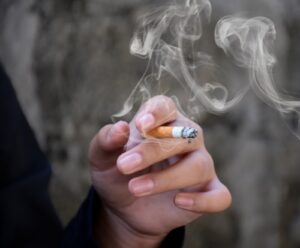 Closeup hand holding lighted cigarrette of asian smoking boy in private area of school and house to avoid punishment from teachers or parents, new edited.